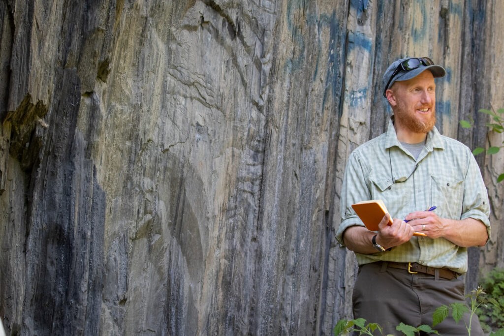An adult student with notebook taking notes in front of quarry wall