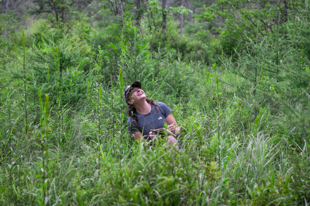 adult naturalist student sitting in a bog smiling and looking towards the sky