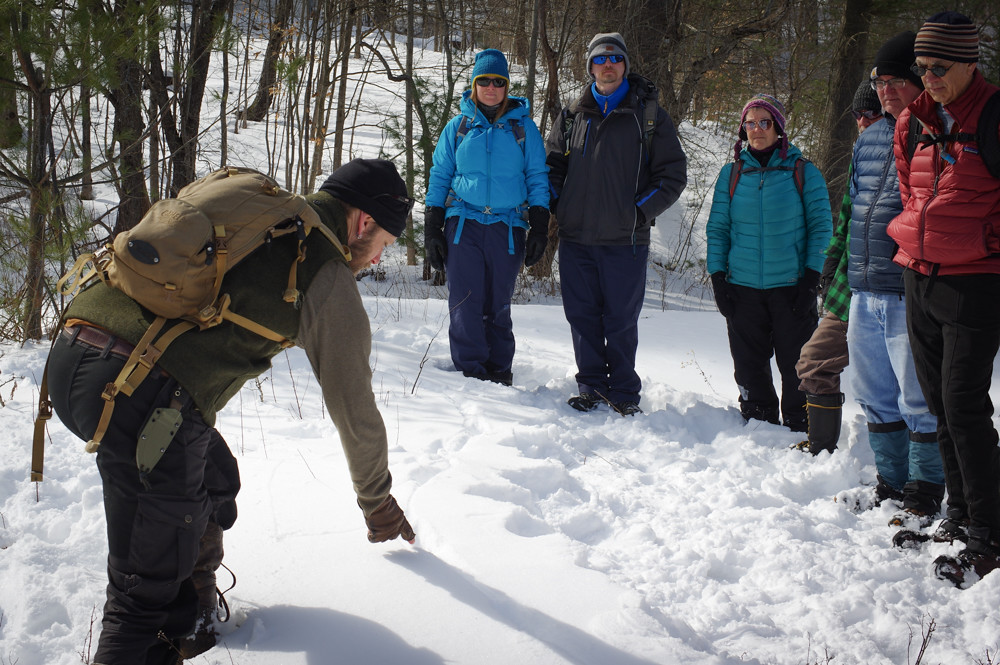 nbnc instructor pointing at animal tracks in snow while group watches