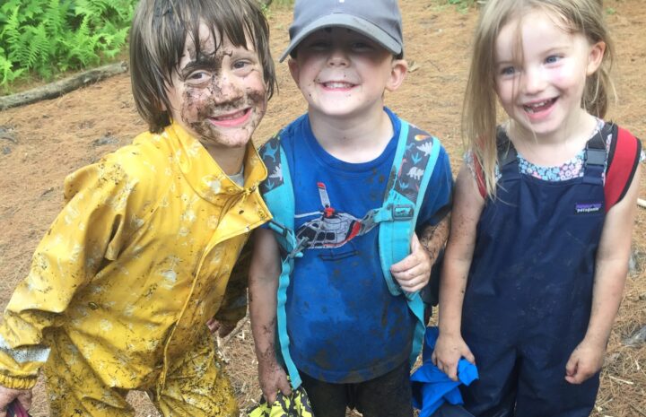 three muddy preschoolers smile at the camera