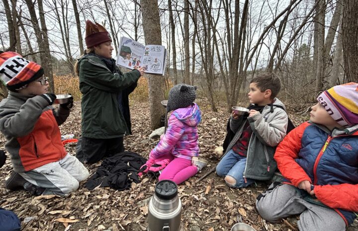 a teacher reads a book to students in the stick season woods
